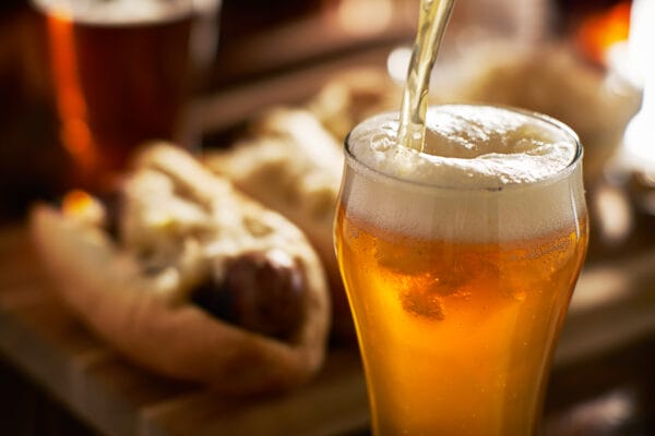 pouring amber beer into mug with bratwursts in background