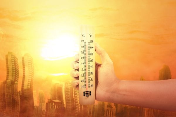Hand holding thermometer with high temperature on the city with glowing sun background