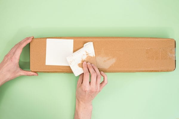 Hands peel off the label from a long paper parcel on a light green background